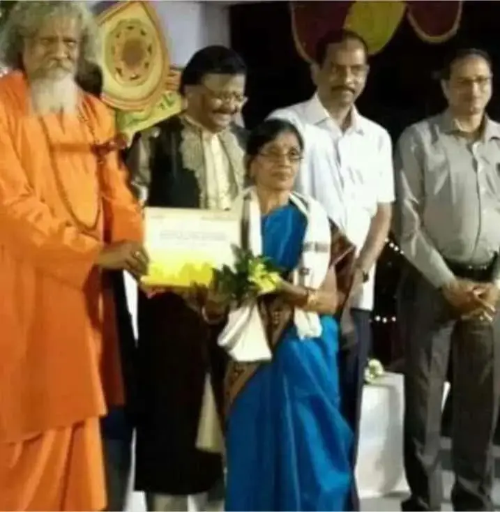 Basanta Kumari Samanta receiving a citation from a saffron-robed dignitary, flanked by other guests on stage